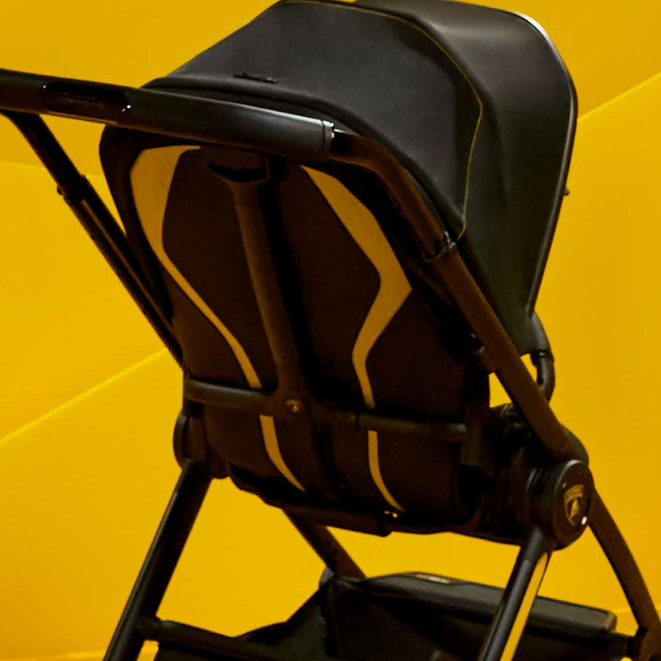 A black stroller with gold accent stripes, positioned on a bright yellow geometric studio background.