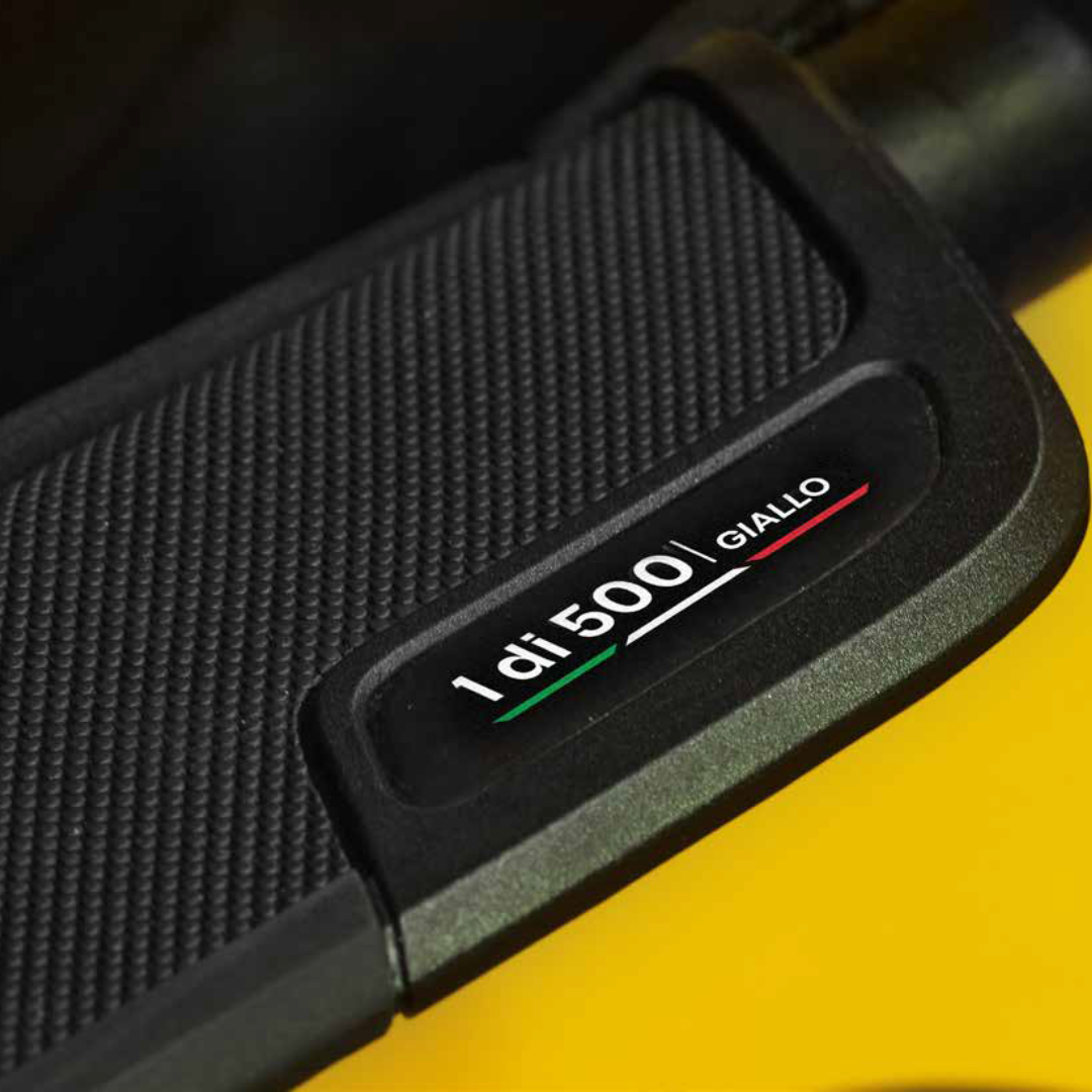 Close-up of a black textured motorcycle handlebar grip with a badge reading '1 di 500 GULLO' in white, green, and red text, set against a bright yellow background.