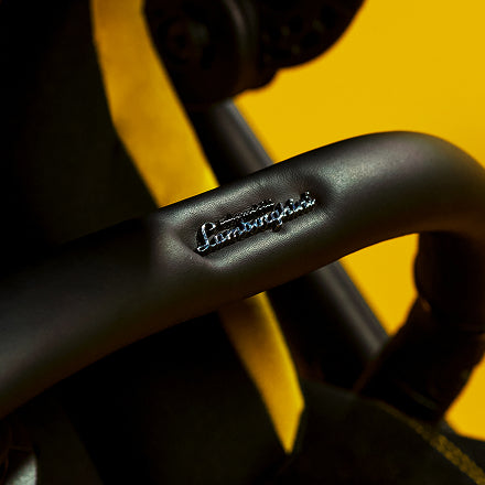 Close-up of a matte black Lamborghini handlebar with the brand name embossed in silver, set against a bright yellow background.